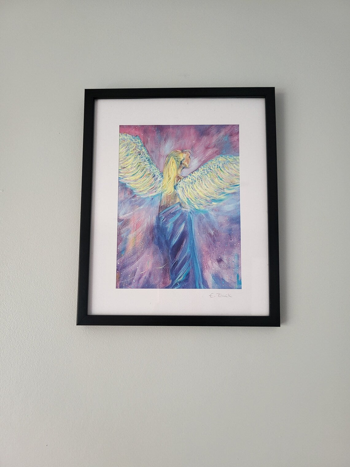 An A5 giclee fine art print of an angel painting, with a visible black frame, hanging on a wall.