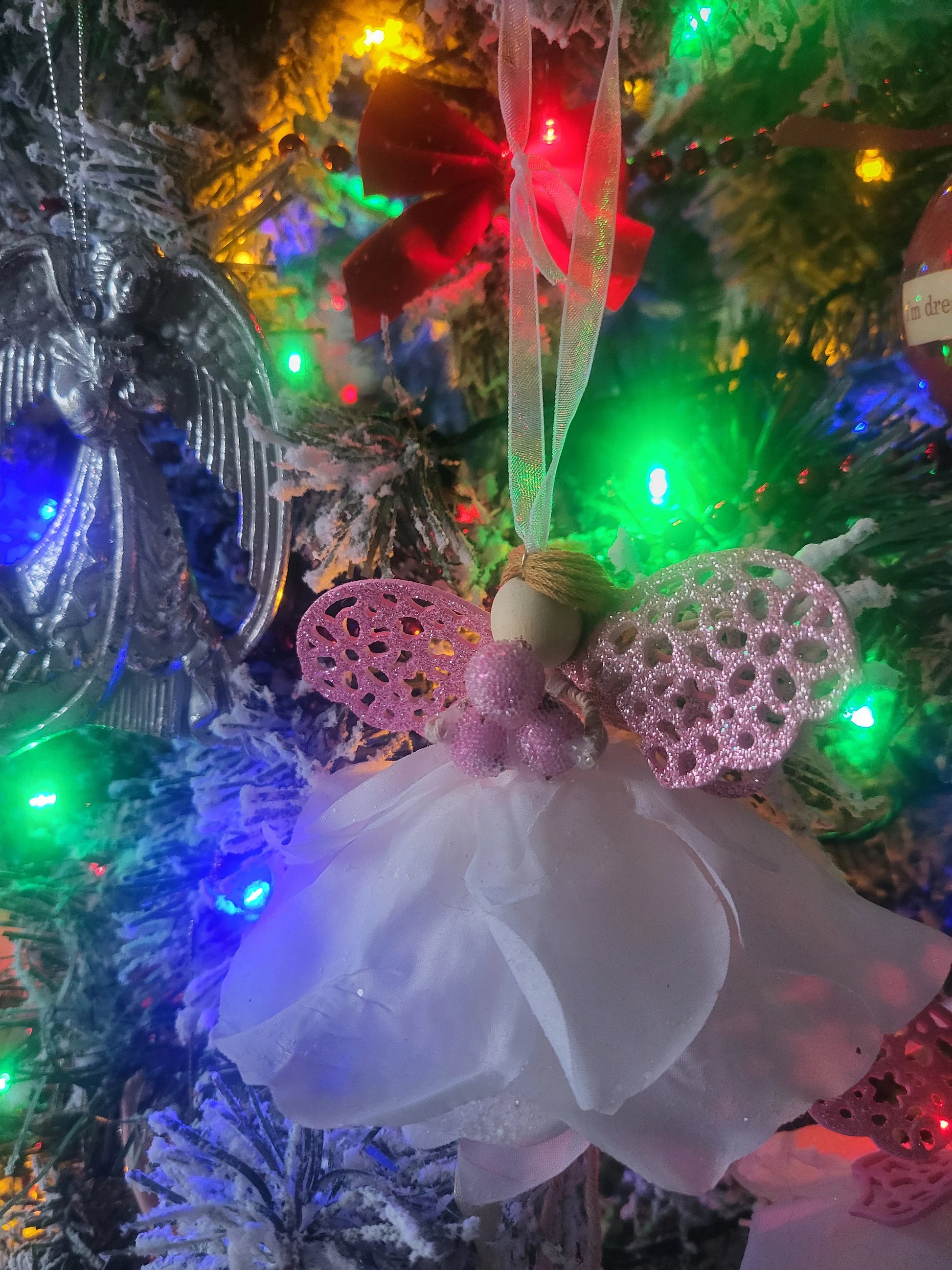 Decorative angel ornament with pink wings and white dress on a Christmas tree with colorful lights.