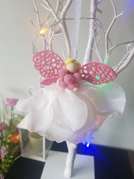 Fairy decoration with pink wings and white skirt on a branch against a neutral background