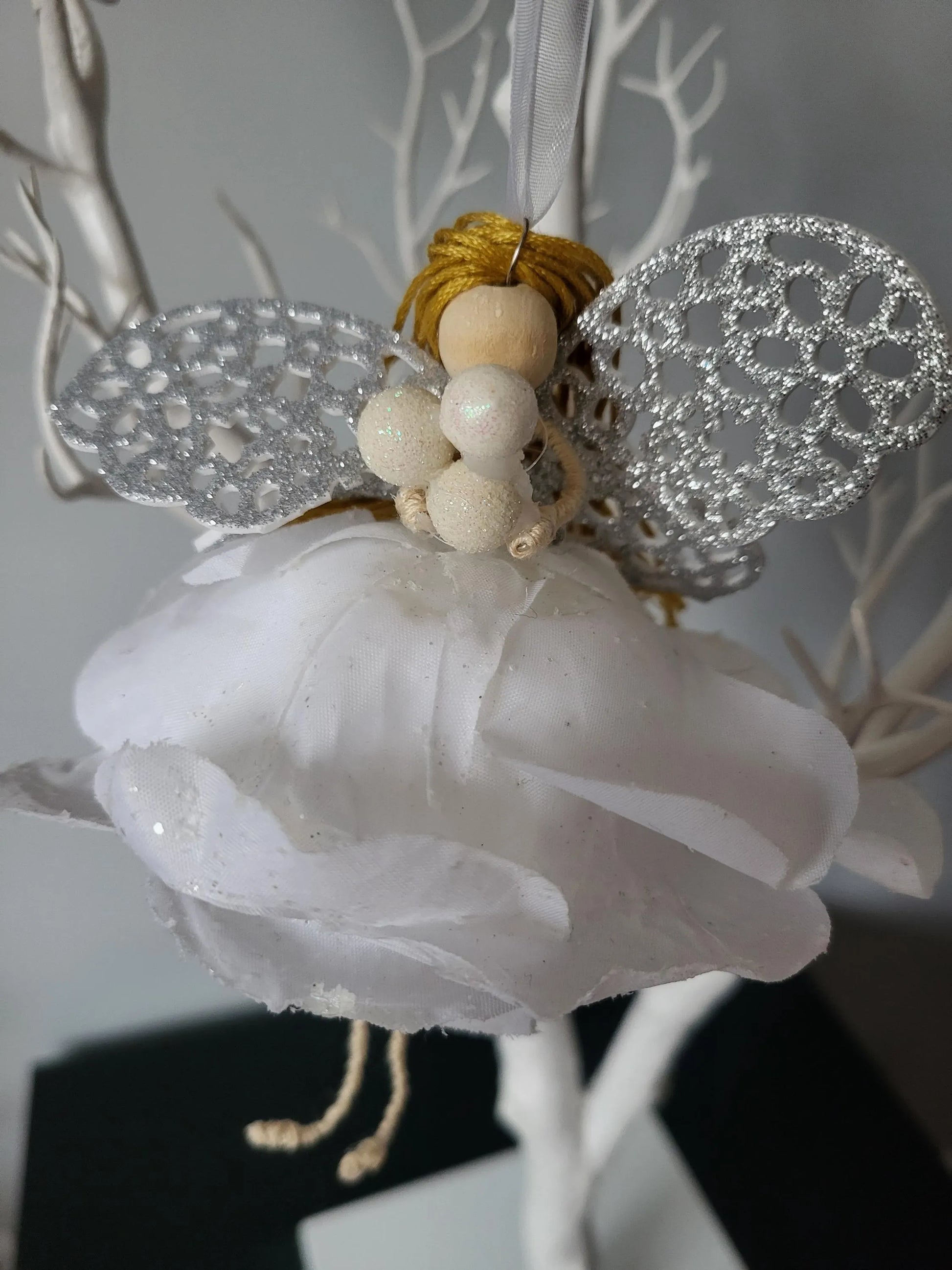 Decorative fairy figure with white wings and body, gold hair, and pearl-like beads on a branch.