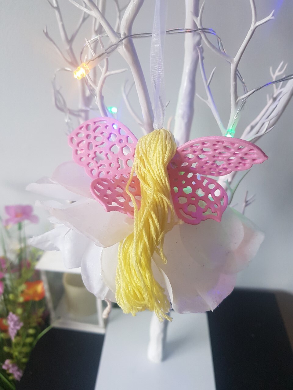 Decorative butterfly with pink and yellow wings on a white branch against a light background