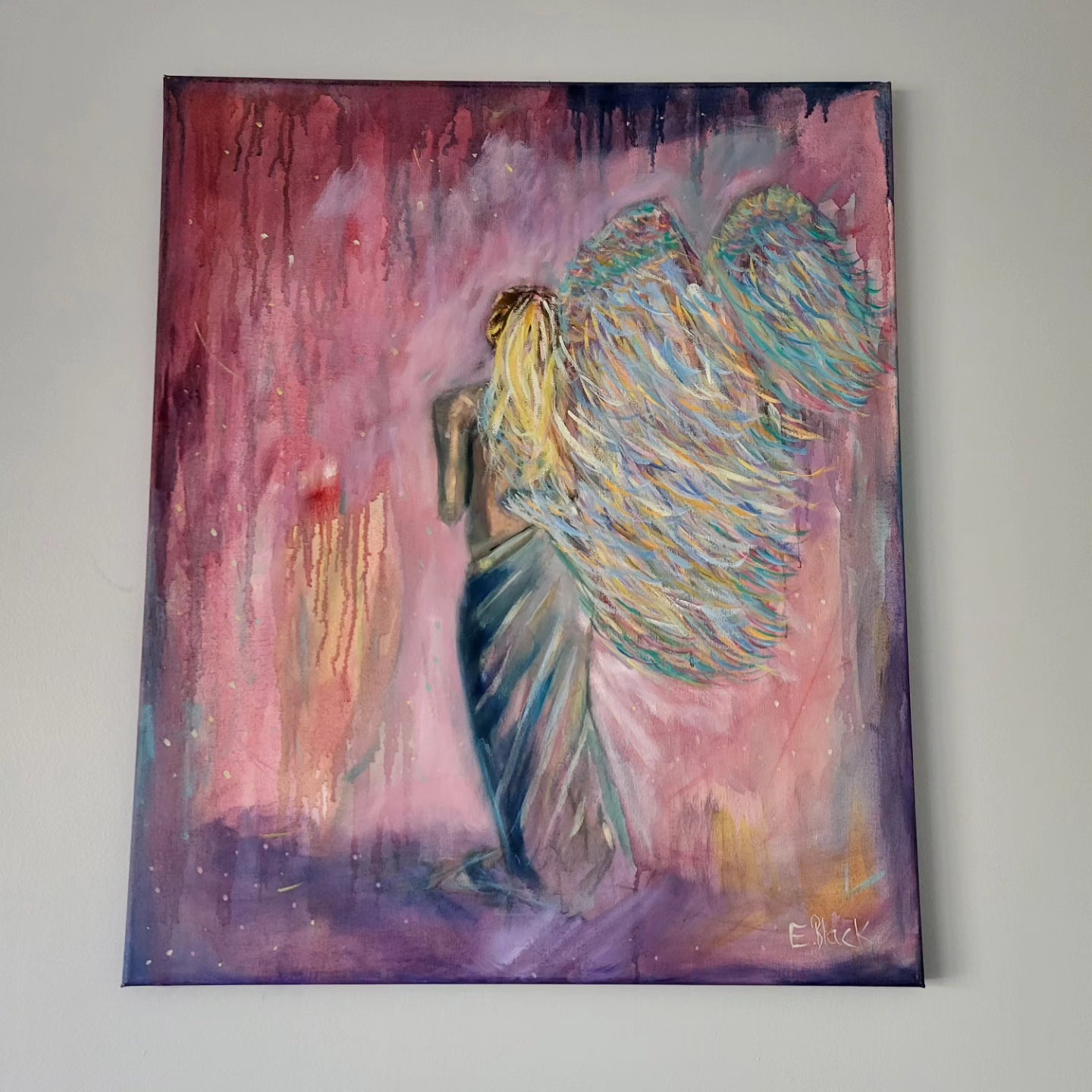 Original oil painting of a standing angel figure with multicolored wings on a pink and purple background, signed by artist Emmalouise B Art.