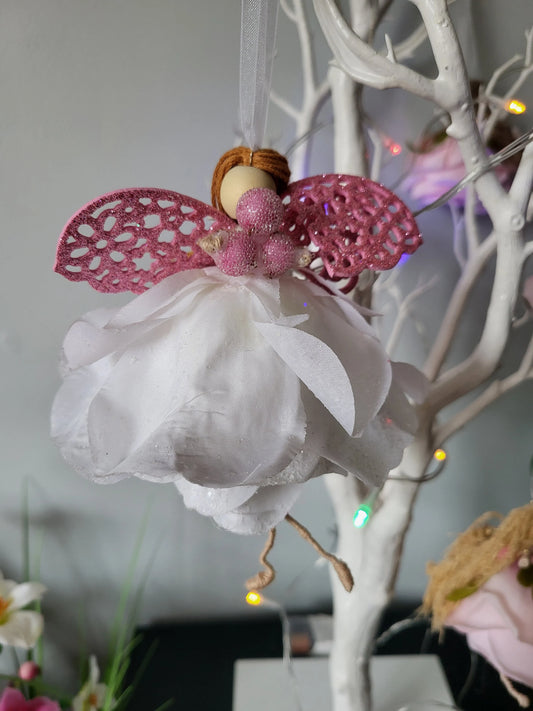 Decorative angel figurine with pink wings and white dress hanging on a branch.